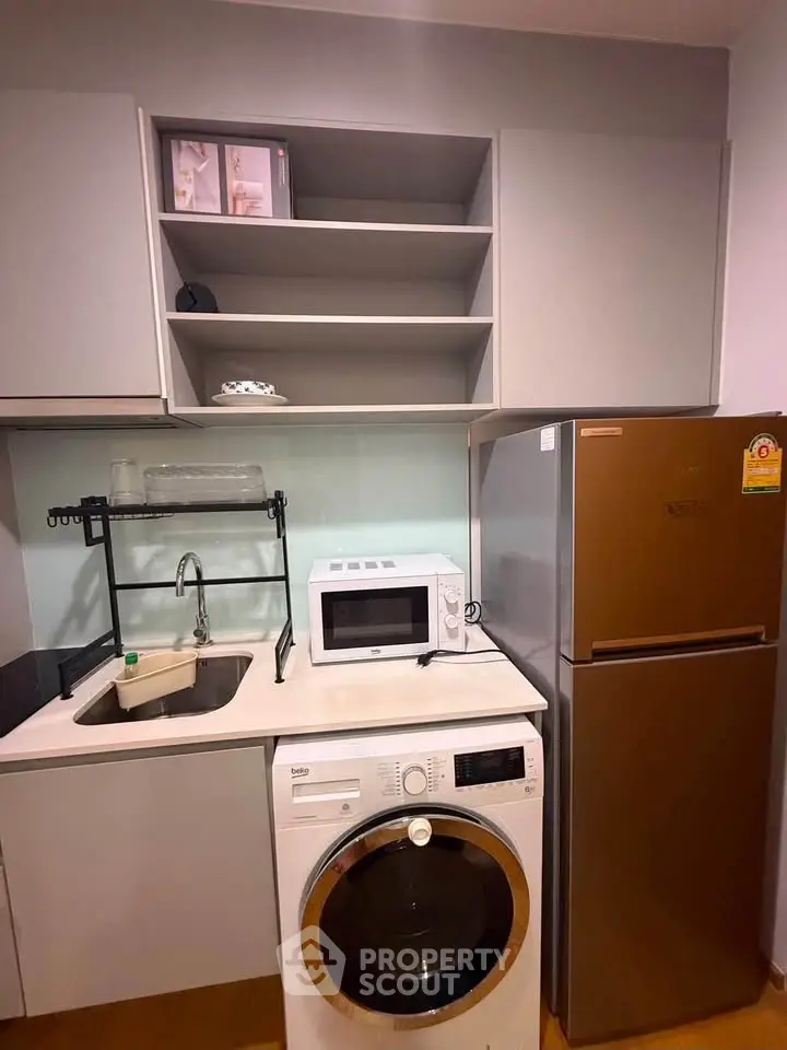 Modern kitchen with washing machine, microwave, and fridge in compact layout.