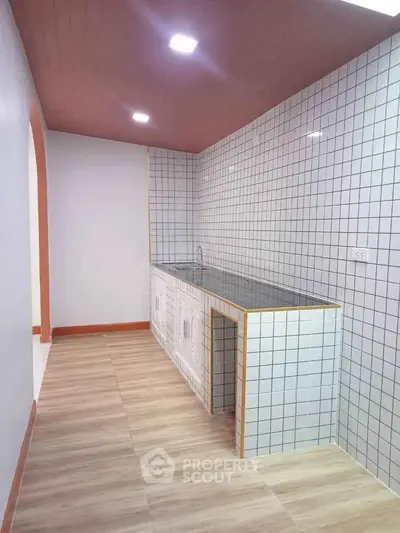 Modern kitchen with tiled walls and wooden flooring, featuring a sleek countertop.