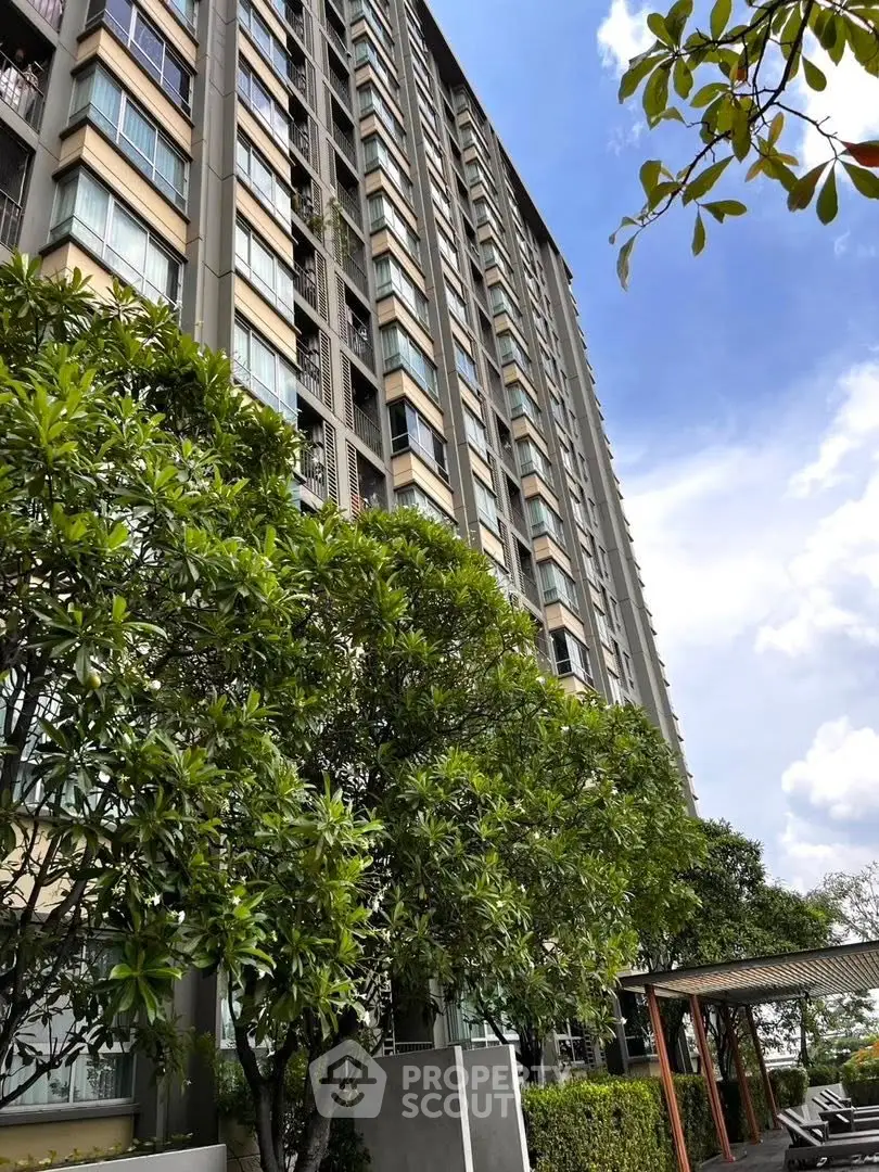 Modern high-rise building with lush greenery and clear blue sky, perfect for urban living.