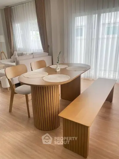 Modern dining area with wooden table and bench, elegant curtains, and cozy seating in a bright living space.