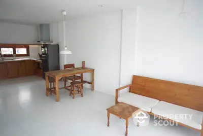 Minimalist open-plan living and dining area with wooden furniture and white walls, offering a cozy and modern ambiance.