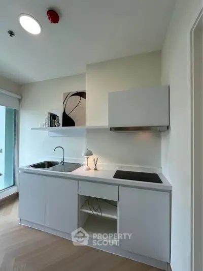 Modern minimalist kitchen with sleek white cabinetry and open shelving, featuring a compact design and natural light.