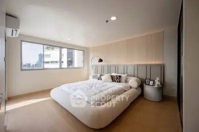 Spacious modern bedroom with large windows and elegant decor in a city apartment.