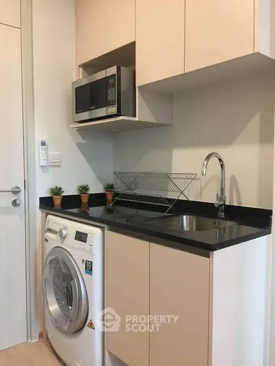 Modern compact kitchen with washing machine and microwave in sleek apartment.