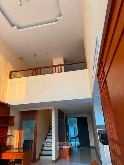 Spacious modern living room with high ceiling and mezzanine, featuring elegant wooden accents and natural light.