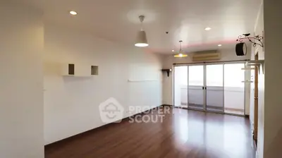 Spacious empty living room with wooden flooring and balcony access in modern apartment.