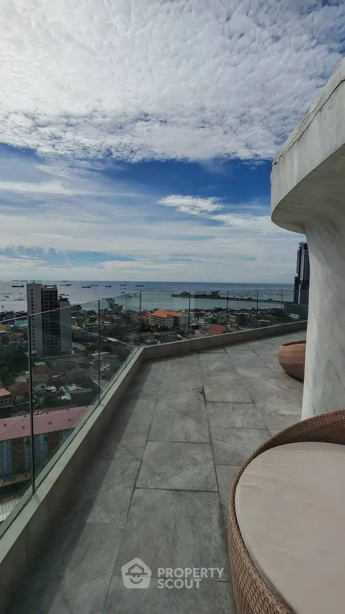 Stunning rooftop view with ocean and cityscape, featuring modern glass railing and stylish seating.