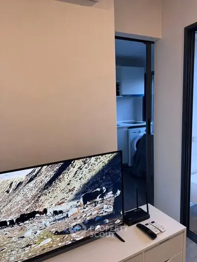 Modern apartment interior with TV and glimpse of kitchen with washing machine.