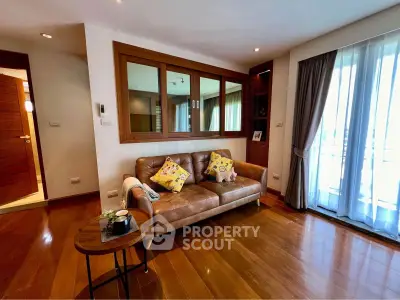 Charming living room with leather sofa and wooden flooring, featuring large windows for natural light.