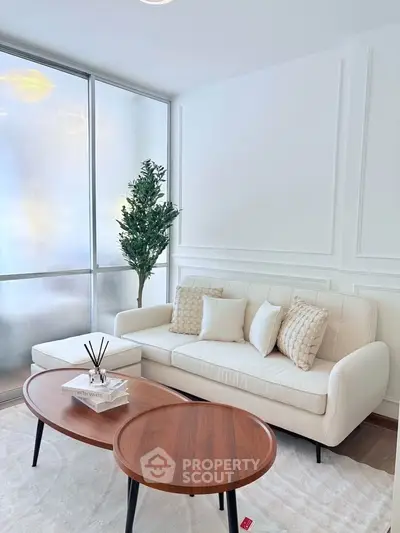 Elegant living room with white sofa, modern coffee tables, and decorative plant.