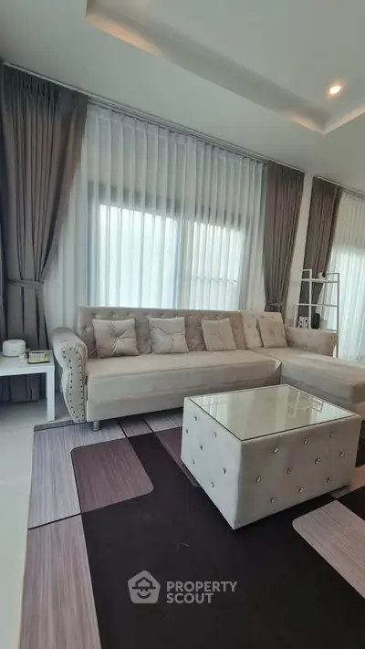 Elegant living room with plush sofa and modern decor, featuring large windows and stylish curtains.
