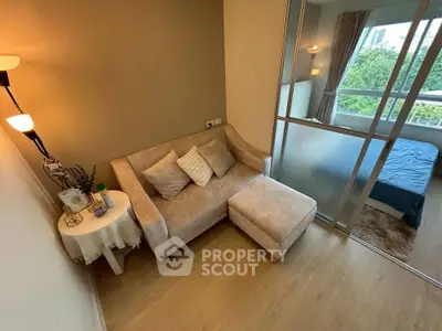 Modern living room with cozy sofa and view into bedroom through glass partition.