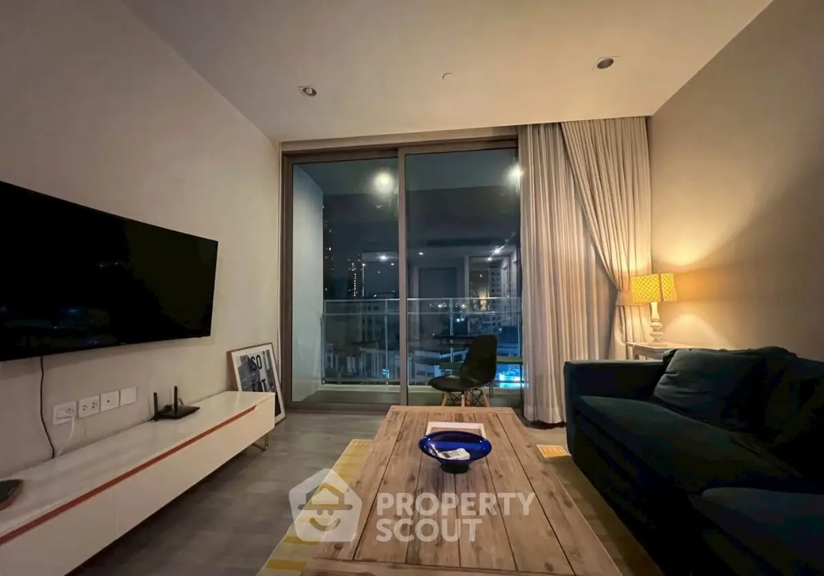 Modern living room with large glass doors leading to a balcony, featuring cozy seating and ambient lighting.
