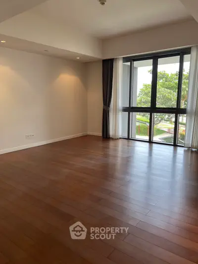Spacious empty living room with large windows and wooden flooring.