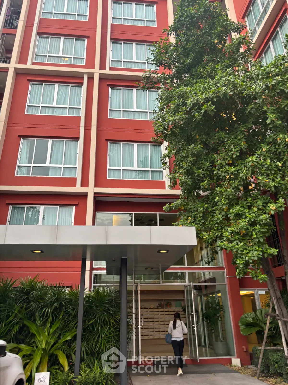 Modern red apartment building with lush greenery and glass entrance