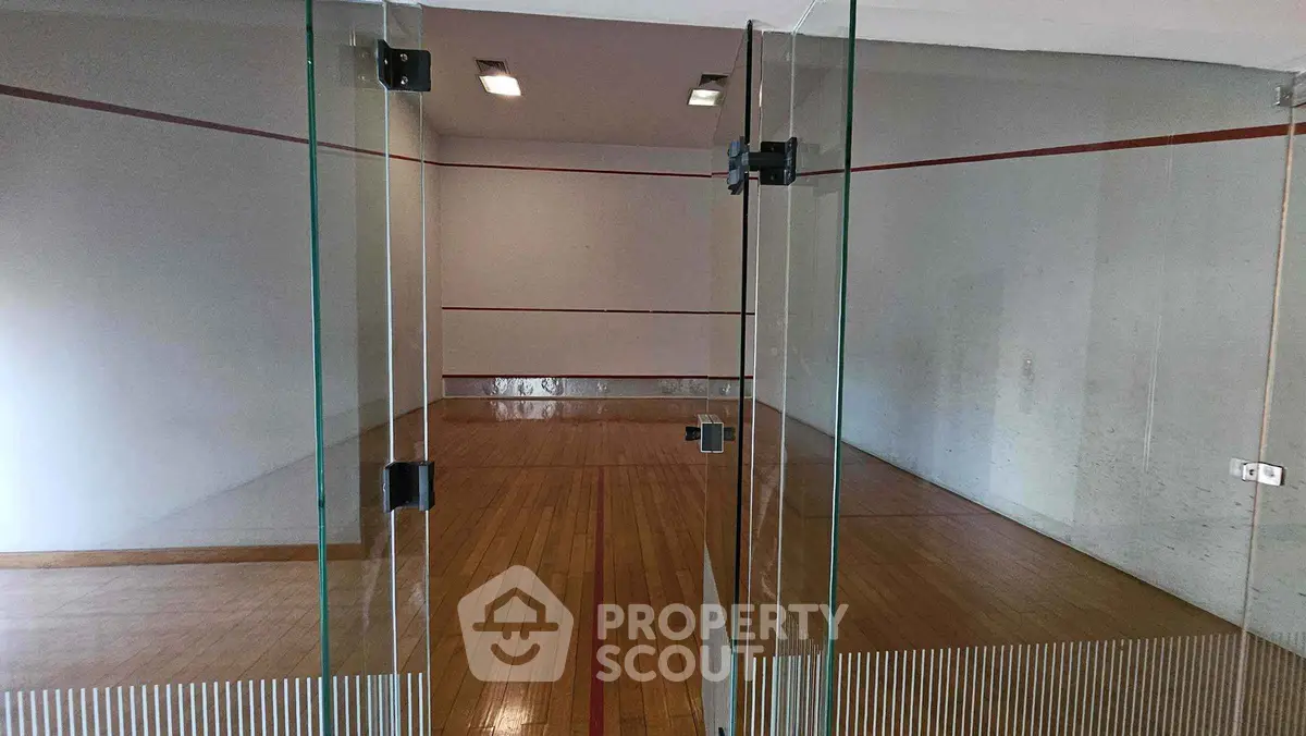 Spacious indoor squash court with wooden flooring and glass doors in a modern residential complex.