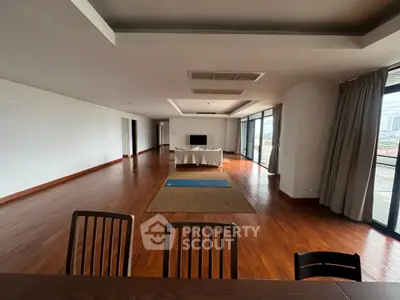 Spacious open-plan living room with wooden flooring and large windows offering city views.