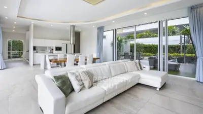 Spacious modern living room with open kitchen and garden view, featuring elegant white sofa and large windows.