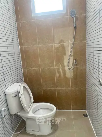 Modern bathroom with sleek tiles and showerhead, featuring a compact toilet design.