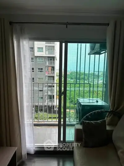 Modern apartment living room with balcony view overlooking greenery and cityscape.
