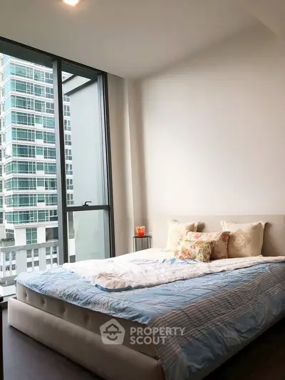 Modern bedroom with large window and city view in a high-rise apartment.