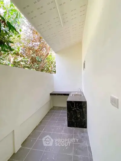 Chic outdoor kitchenette with sleek black marble countertop and lush greenery view.