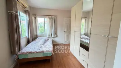 Cozy bedroom with wooden flooring and large windows offering natural light and garden views.