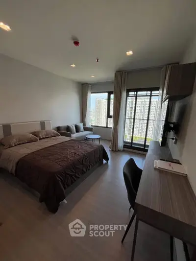 Modern bedroom with city view, featuring a cozy bed, desk, and large windows for natural light.