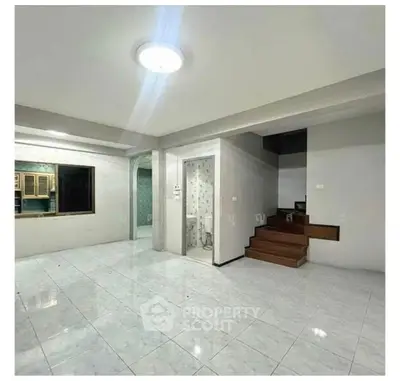 Spacious open-plan living area with tiled flooring and modern lighting, featuring a small staircase and adjacent kitchen.