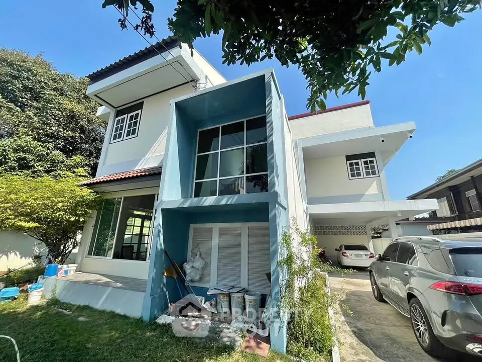 Spacious two-story house with large windows and driveway in a lush green setting.
