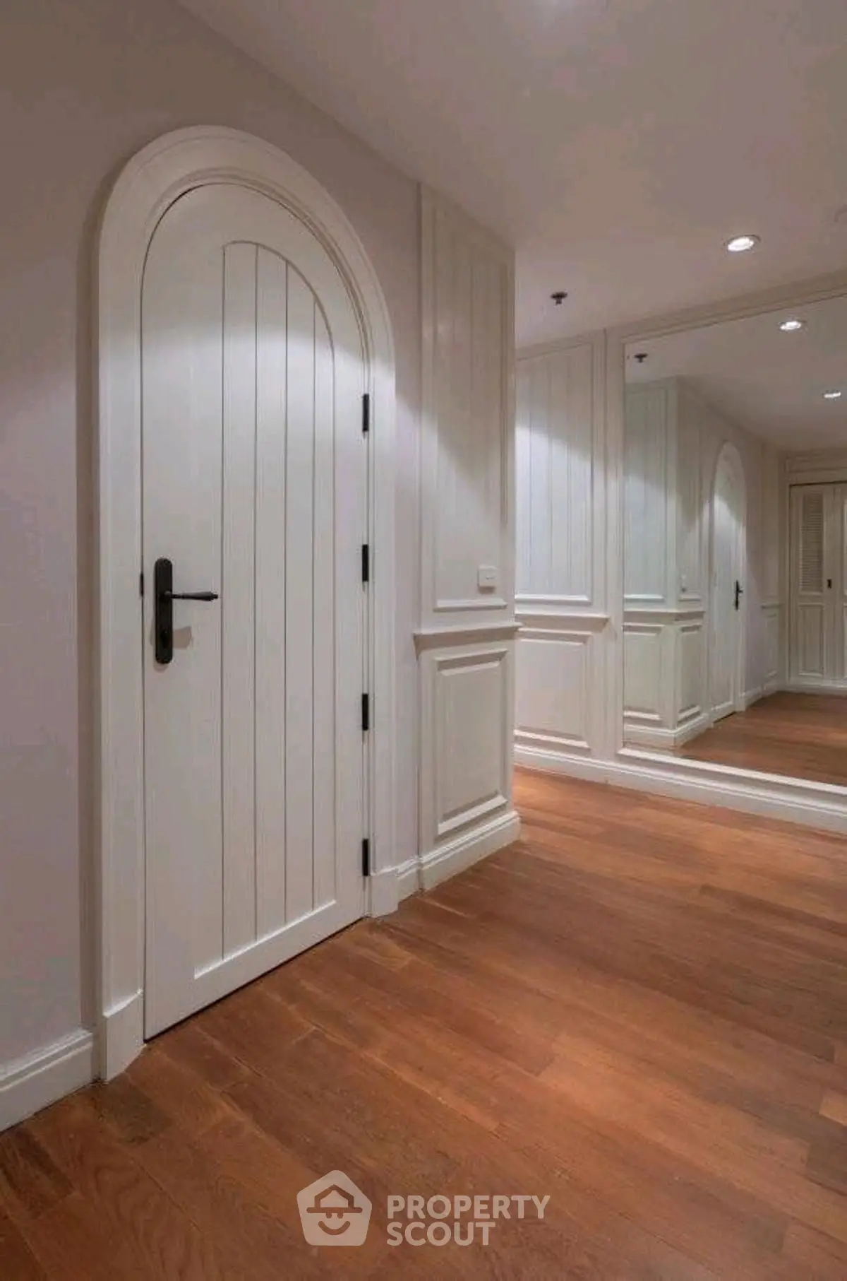 Elegant hallway with wooden floors and arched door, featuring mirrored wall panels.