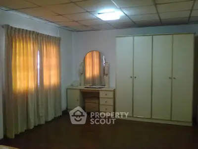 Spacious bedroom with ample natural light, hardwood floors, large wardrobe, and a vintage vanity dresser.
