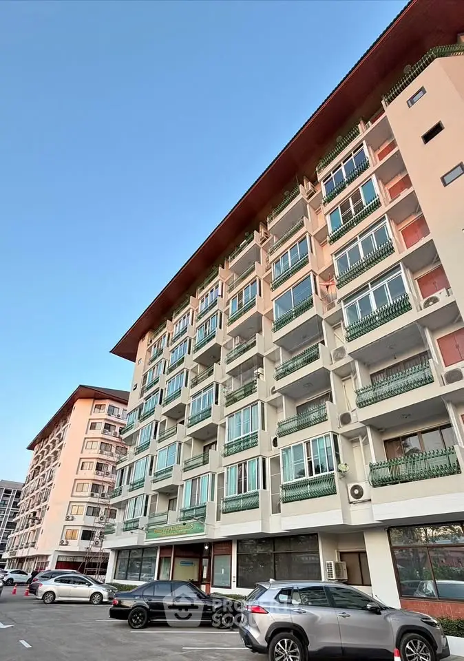 Modern multi-story residential building with balconies and parking area, showcasing urban living.