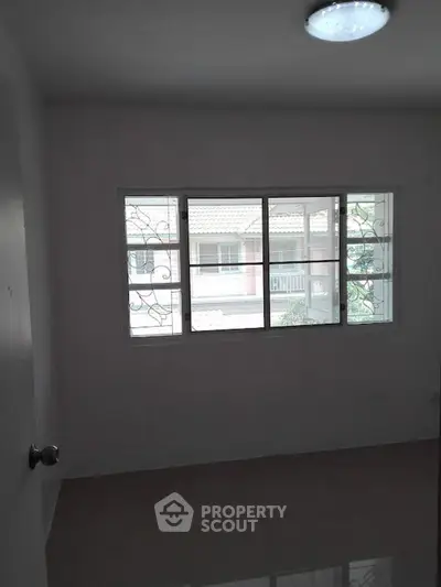 Bright room with large window and view of neighboring houses, perfect for customization.
