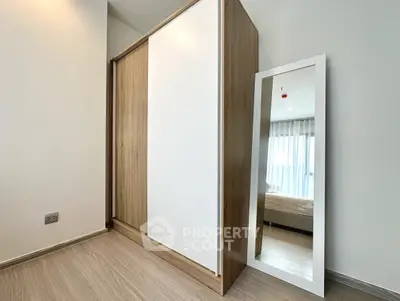 Modern bedroom with sleek wardrobe and full-length mirror, featuring natural light and minimalist design.
