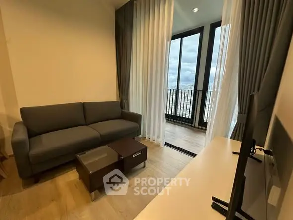 Modern living room with large windows and balcony view, featuring a cozy sofa and sleek TV setup.