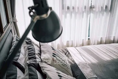 Cozy bedroom with stylish bedding and natural light through sheer curtains.