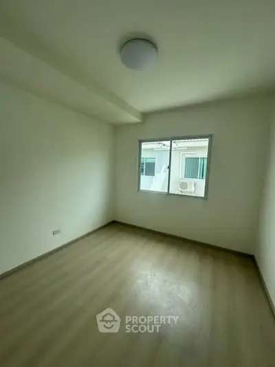 Spacious empty bedroom with wooden flooring and large window