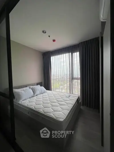 Cozy bedroom with large window offering natural light and city view, featuring a comfortable bed and modern decor.