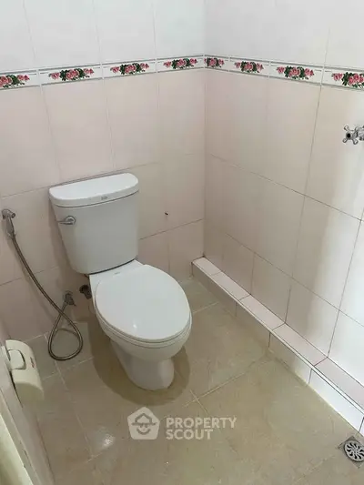 Compact bathroom with tiled walls and floor, featuring a toilet and bidet spray.