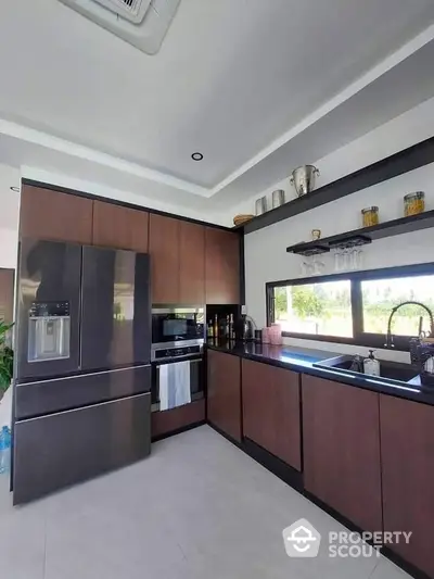 Spacious modern kitchen with sleek dark wood cabinetry, stainless steel appliances, and a large window offering ample natural light.