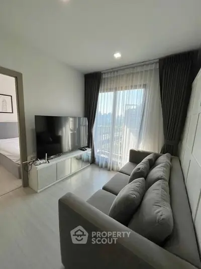 Modern living room with sleek design and large TV, featuring a cozy gray sofa and floor-to-ceiling windows.