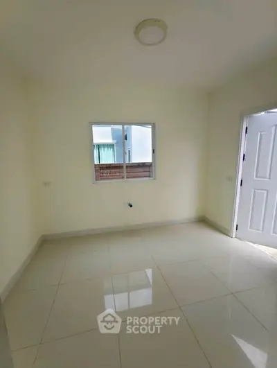 Spacious empty room with glossy tiled floor and natural light from window.