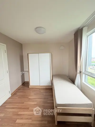 Minimalist bedroom with wooden flooring and large window offering natural light.