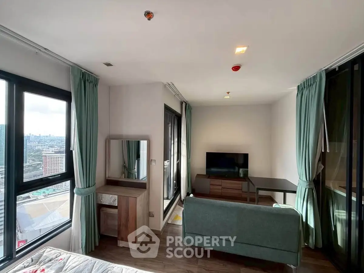 Modern living room with large windows offering city views, featuring stylish furniture and natural light.