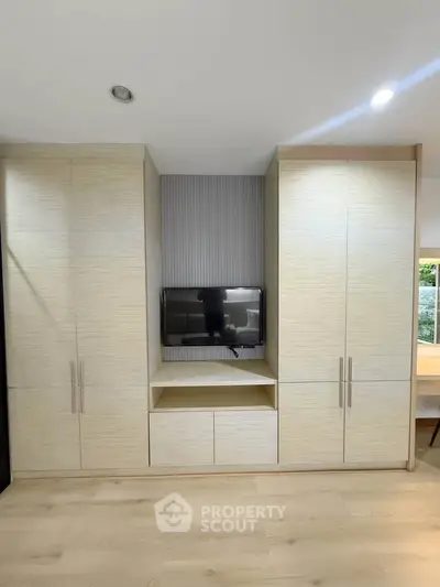 Modern living room with built-in storage and TV, featuring sleek design and ample natural light.
