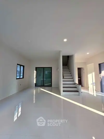 Spacious modern living room with sleek staircase and large windows, perfect for natural light lovers.