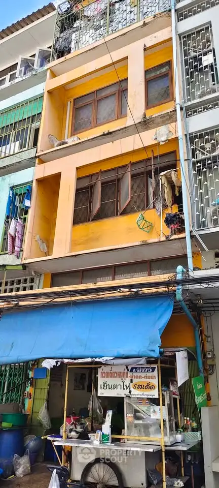 Vibrant yellow multi-story building with street food stall in urban setting.