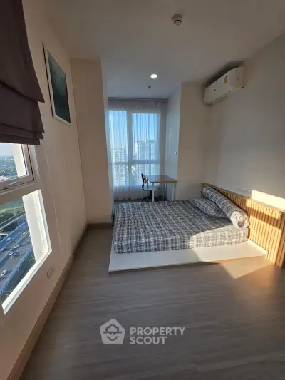 Bright bedroom with large windows and city view, featuring a cozy bed and air conditioning unit.