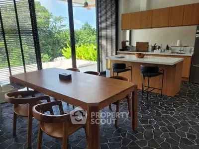 Modern kitchen with open layout and stylish dining area, featuring sleek black flooring and large windows.